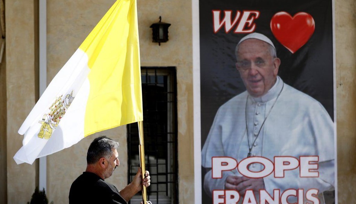 كاهن عراقي يحمل علم الفاتيكان أمام كنيسة مار يوسف في بغداد استعداداً لزيارة البابا فرنسيس، 26 شباط 2021 - "أ ب"