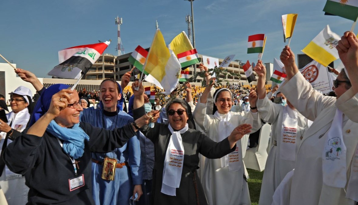 راهبات يلوحن بأعلام العراق وكردستان العراق والكرسي الرسولي في انتظار وصول البابا فرنسيس إلى ملعب فرانسو الحريري في إربيل (7 آذار 2021، أ ف ب). 