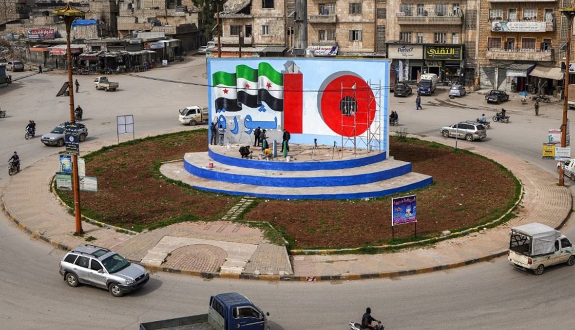 ناشطون رسموا جدارية عند مستديرة مدينة إدلب السورية في الذكري العاشرة للإنتفاضة على النظام.(أ ف ب)