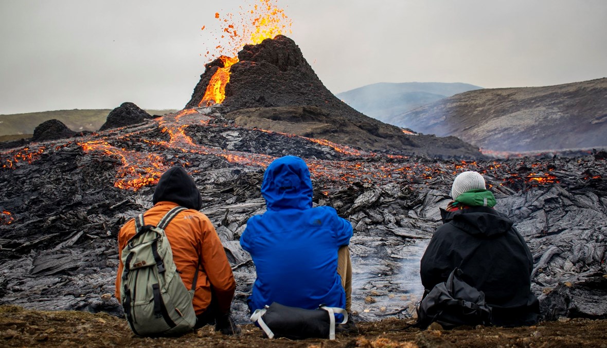 ينظر المتنزهون إلى الحمم البركانية المتدفقة من البركان المنفجر على بعد حوالى 40 كيلومتراً غرب العاصمة الأيسلندية، في 21 آذار 2021 (تعبيرية – أ ف ب).
