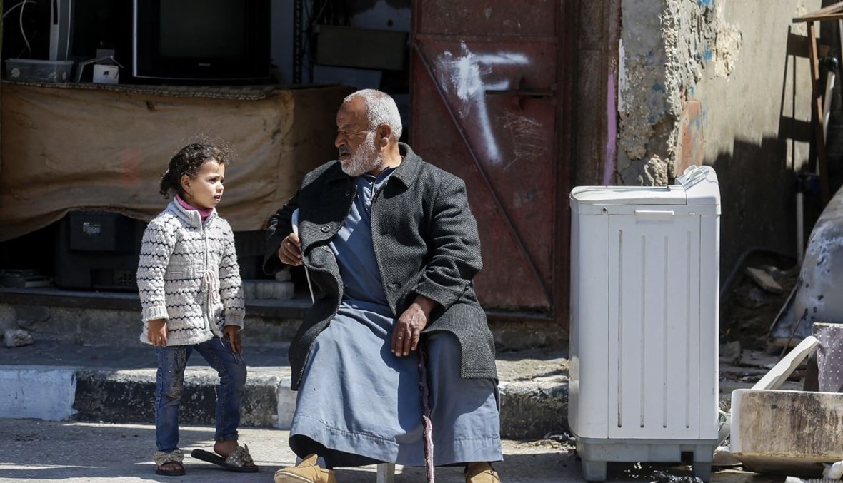 رجل فلسطيني مسن يتحدث الى طفلة خلال جلوسه أمام متجر في بلدة خان يونس جنوب قطاع غزة (25 آذار 2021، أ ف ب). 
