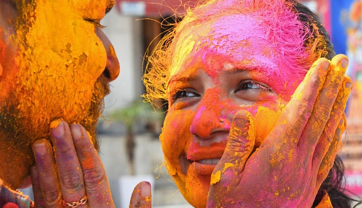 شخصان يضحكان، بينما تمرمغ وجهاهما بمسحوق ملون يستخدم في احتفالات مهرجان هولي الربيعي الهندوسي الشهير، في أحد المعابد في أمريتسار بالهند (28 آذار 2021، أ ف ب). 