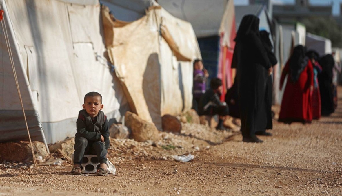 طفل يجلس بالقرب من نازحين سوريين انتظروا بالصف للحصول على وجبة الإفطار الرمضانية في مخيم في بلدة سرمدا في محافظة إدلب شمال غرب سوريا (13 نيسان 2021، أ ف ب). 