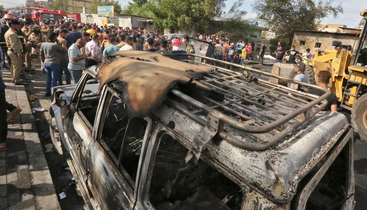 أشخاص تجمعوا حول سيارة مدمرة في موقع الانفجار في حي الحبيبية بضاحية مدينة الصدر في بغداد (15 نيسان 2021، أ ف ب).