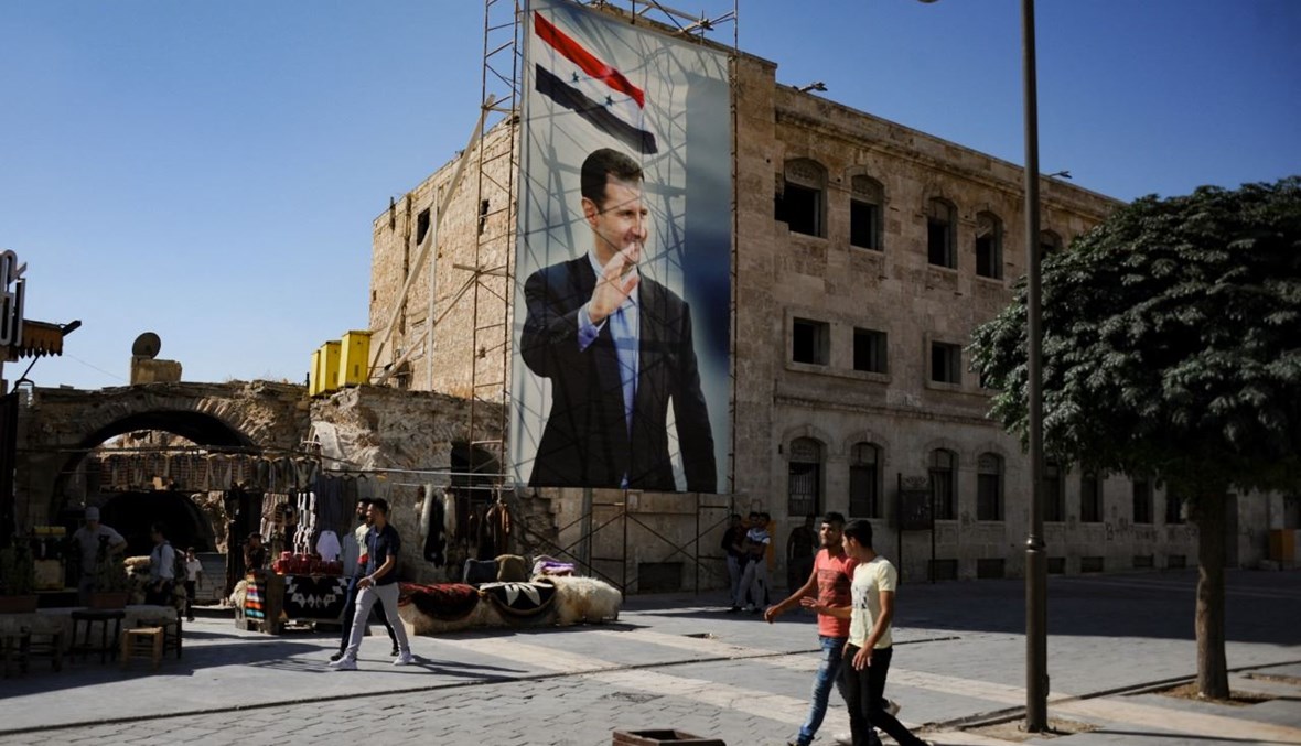رجال يمرون بالقرب من ملصق للرئيس الأسد في مدينة حلب القديمة (27 ايلول 2019، أ ف ب). 