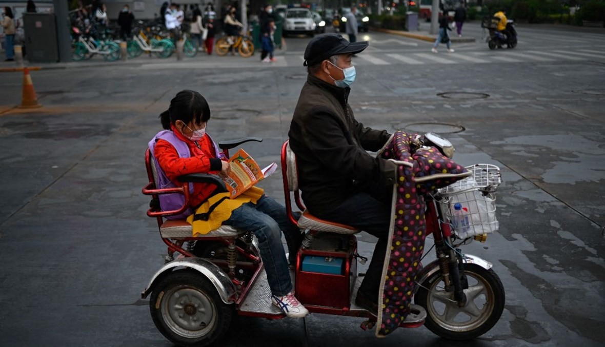 طفل يجلس على ظهر دراجة كهربائية في أحد شوارع بيجينغ (25 نيسان 2021، أ ف ب).