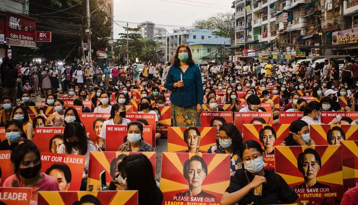 متظاهرون يحملون لافتات تظهر صورة الزعيمة المدنية الميانمارية المحتجزة أونغ سان سو كي يجلسون على طول أحد الشوارع قبل إقامة وقفة احتجاجية على ضوء الشموع خلال مظاهرة ضدّ الانقلاب العسكري في يانغون (أ ف ب).