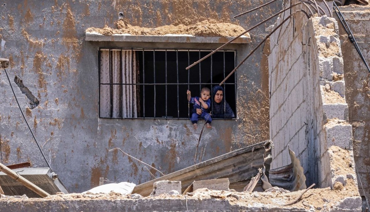 سيدة فلسطينية تحمل طفلها وهي تنظر من نافذة منزل في خان يونس جنوب قطاع غزة (26 ايار 2021، أ ف ب). 