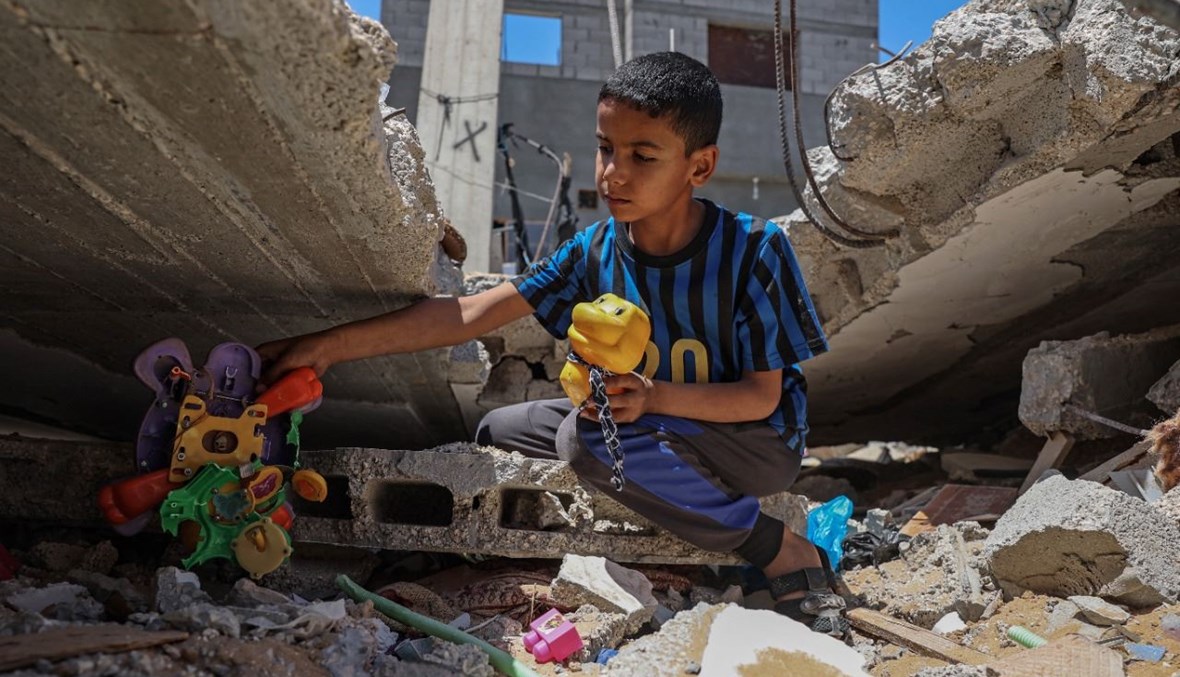 طفل فلسطيني يخرج ألعابه من بين أنقاض منزله الذي دمرته الغارات الإسرائيلية في خان يونس جنوب قطاع غزة (26 ايار 2021، أ ف ب). 