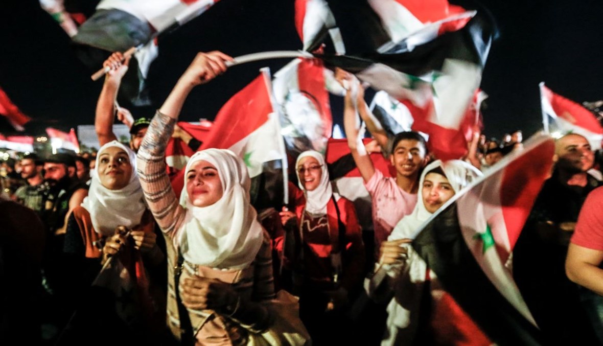 سوريون يلوحون بالأعلام الوطنية وهم يحتفلون في دمشق بفوزه (27 ايار 2021، أ ف ب).