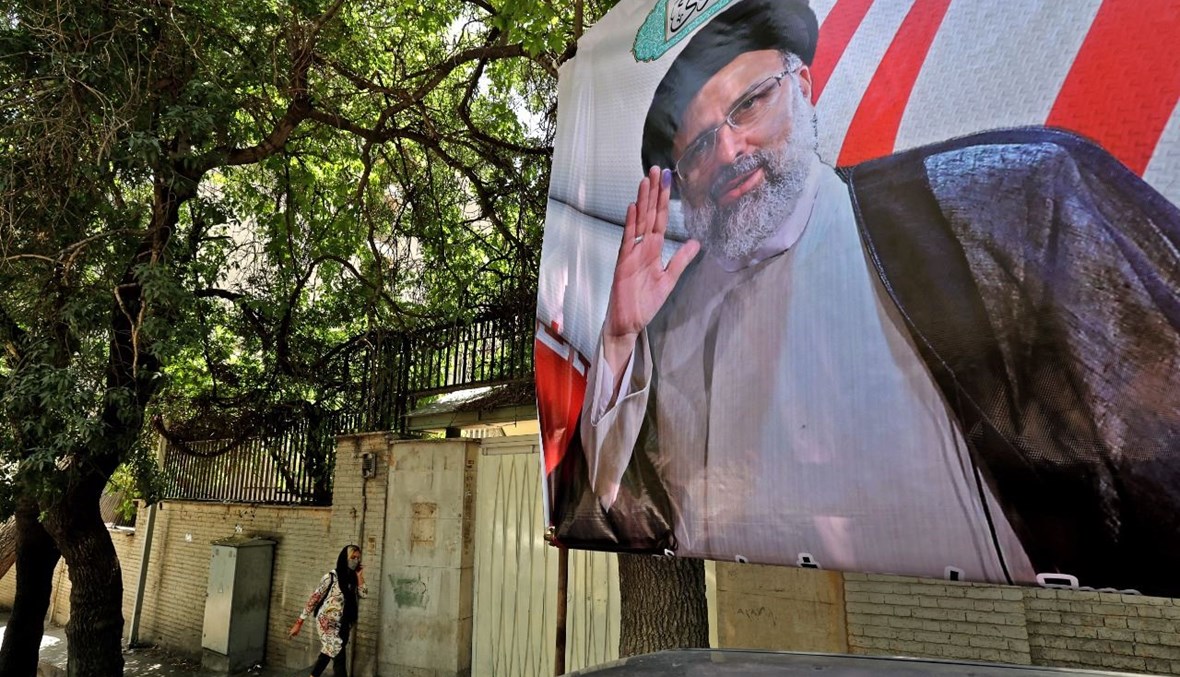 شخص يمر بالقرب من ملصق انتخابي لرئيس القضاء المرشح الرئاسي إبراهيم رئيسي في طهران (1 حزيران 2021، أ ف ب). 