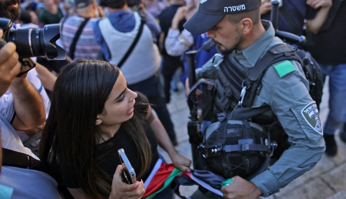 شرطي اسرائيلي ينتزع علماً فلسطينياً من فتاة رفعته في باب العامود بالقدس الشرقية حيث كان المتطرفون الإسرائيليون يقومون بـ"مسيرة الأعلام" أمس.(أ ف ب) 