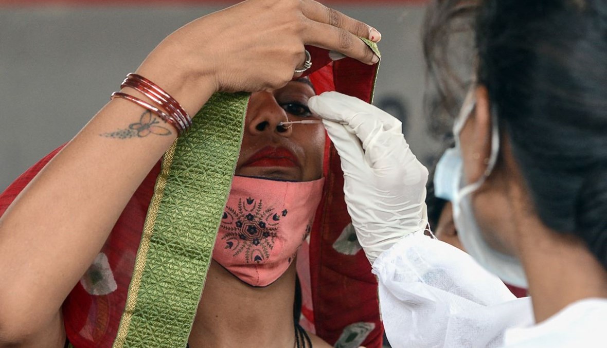 عاملة صحية تأخذ مسحة أنفية من راكبة لدى وصولها إلى محطة قطارات في مومباي بالهند (28 حزيران 2021، أ ف ب).
