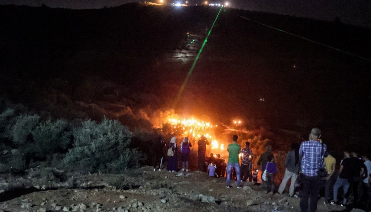 فلسطينيون يستخدمون مشاعل الليزر خلال تظاهرة ليلية في بلدة بيتا  بالقرب من نابلس بالضفة الغربية المحتلة، احتجاجا على بؤرة المستوطنين الإسرائيليين في إفيتار (30 حزيران 2021، أ ف ب). 