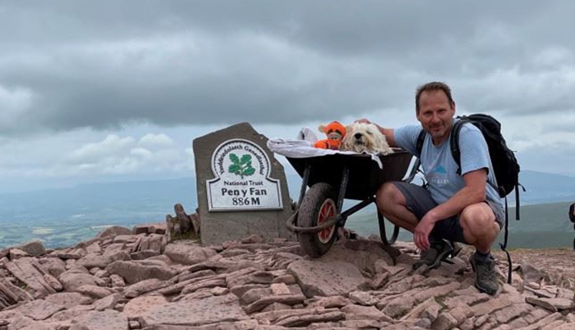 "صديق" يأخذ كلبه المريض إلى أعلى جبله المفضل في عربة يدوية.