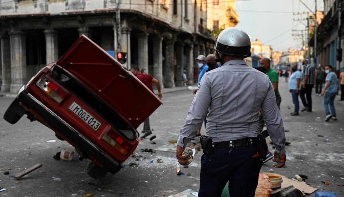 شرطي يقف بالقرب من سيارة مقلوبة تابعة للشرطة في شارع في هافانا خلال تظاهرة ضد الرئيس الكوبي (11 تموز 2021، أ ف ب). 