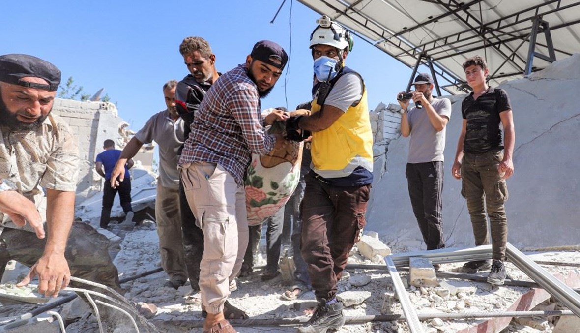 رجال الدفاع المدني من "الخوذ البيض" يحملون جثة قتيل في بلدة إبلين بمحافظة إدلب أمس.    (أ ف ب)