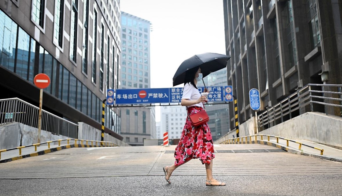 امرأة تمرّ بالقرب من مبنى إداري في بيجينغ (15 تموز 2021، أ ف ب).
