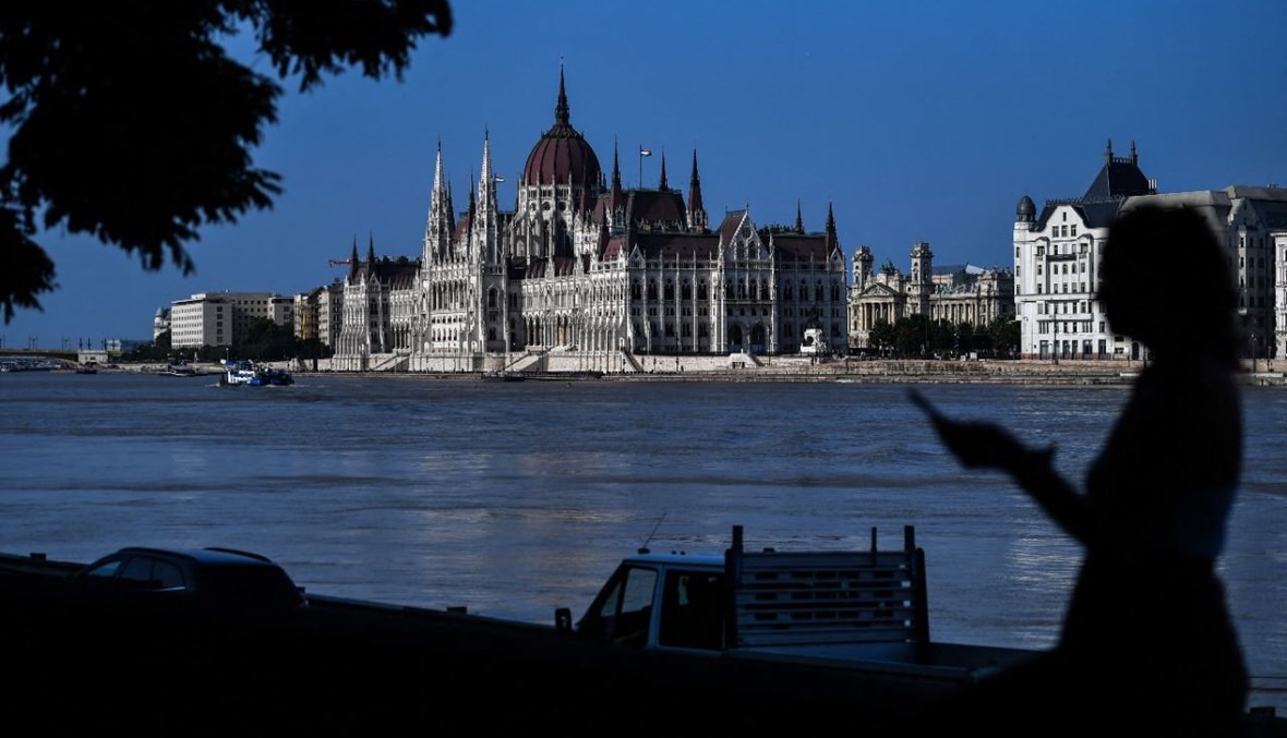 سائح يستخدم هاتفه المحمول عند ضفة نهر الدانوب في بودابست. وبدا البرلمان الهنغاري في الخلفية (20 تموز 2021، أ ف ب). 