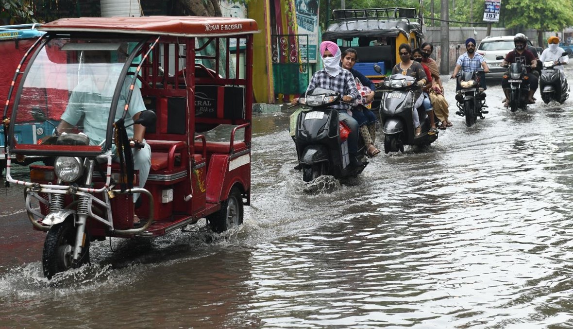 سائقو دراجات نارية يشقون طريقهم في شارع في أمريتسار غارق في السيول بعد هطول أمطار (25 تموز 2021، أ ف ب). 