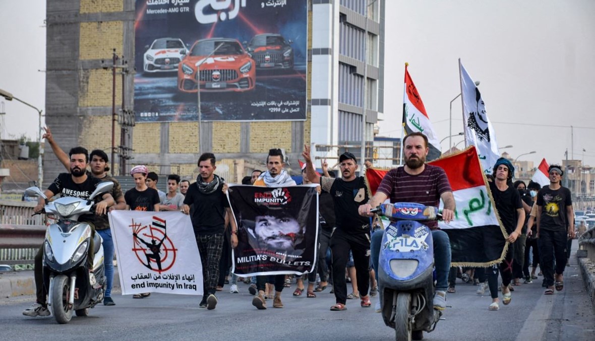 متظاهرون يرفعون لافتات احتجاجية في ساحة الحبوبي بمدينة الناصرية جنوب العراق، تطالب بمحاسبة قتلة عشرات النشطاء (18 تموز 2021، أ ف ب). 