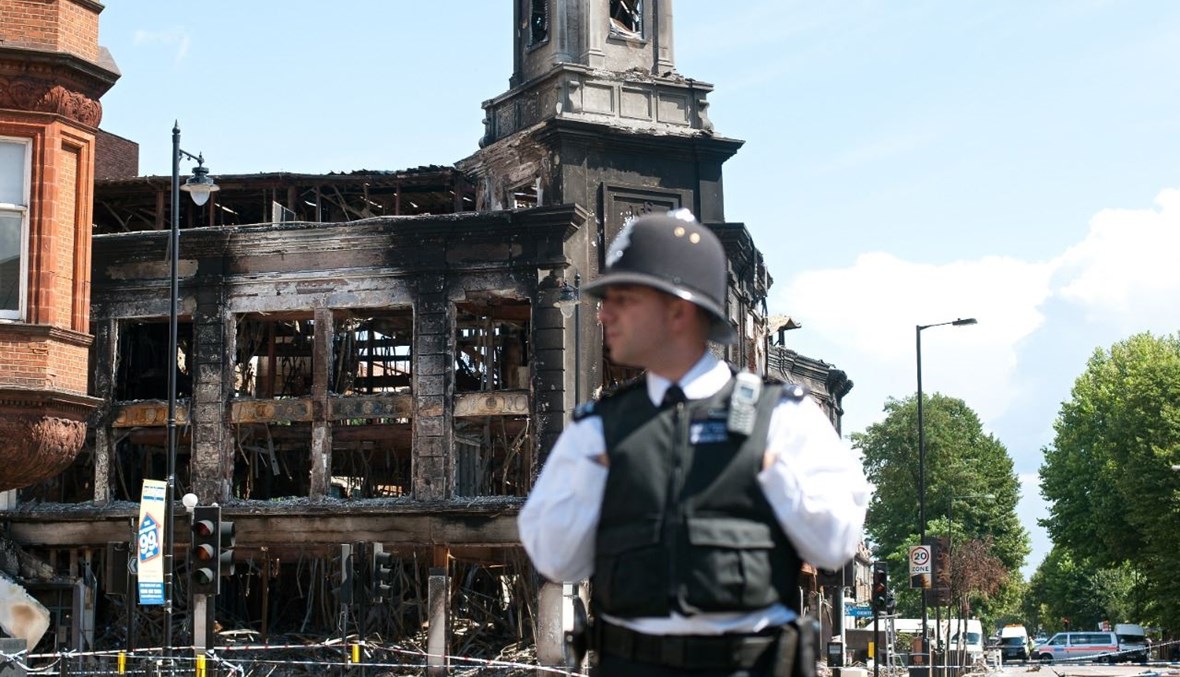 شرطي وقف في أحد الشوارع في توتنهام، حيث بدا خلفه مبنى محترق من جراء أعمال شغب في شمال لندن (8 آب 2011، أ ف ب). 