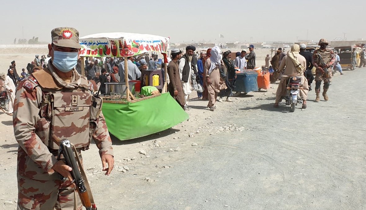جندي افغاني وقف على مقربة من أشخاص ينتظرون إعادة فتح معبر حدودي أغلقته السلطات في شامان (7 آب 2021، أ ف ب). 
