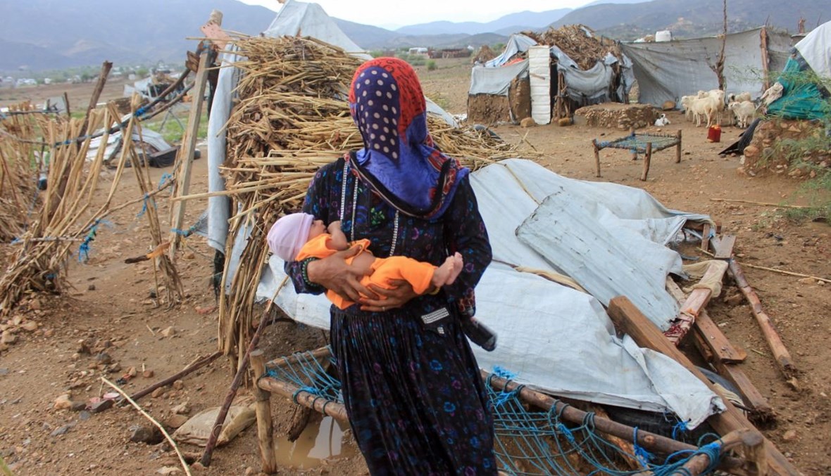 امرأة تحمل طفلها بجوار خيمة دمرتها الأمطار الغزيرة في مخيم موقت لليمنيين النازحين في محافظة حجة الشمالية (7 آب 2021، أ ف ب). 
