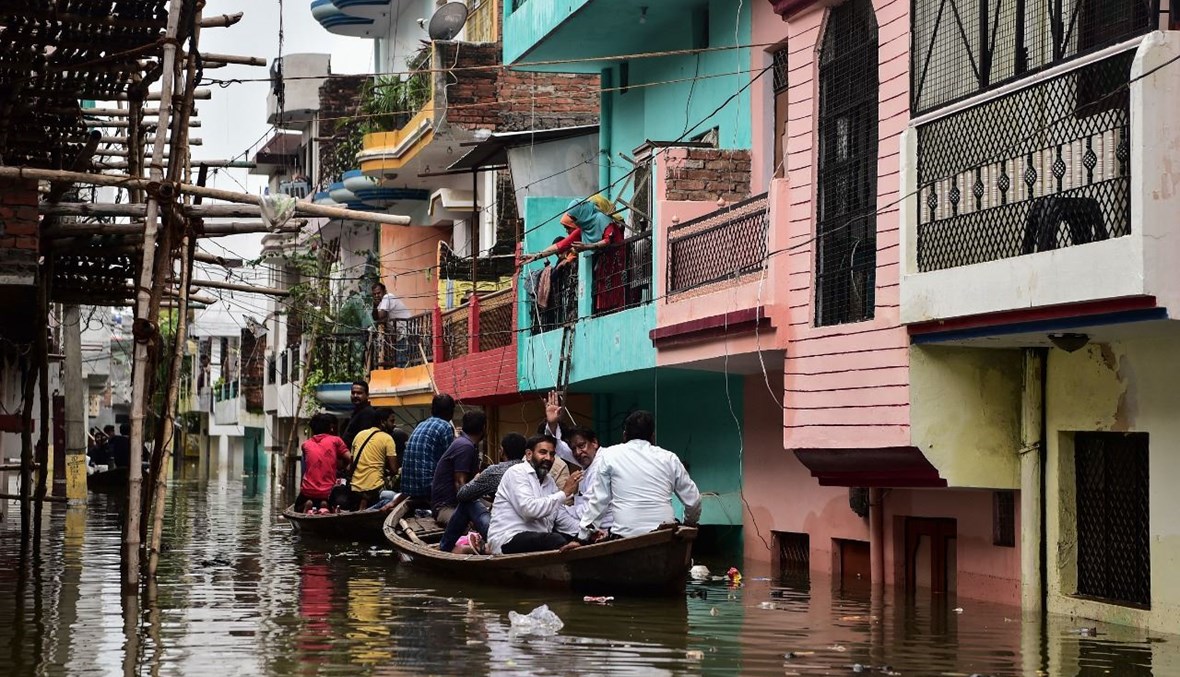 سكان يستخدمون قاربًا للتنقل في حي غمرته المياه في منطقة كاريلي غوس ناغار في مدينة الله أباد بالهند، بعد هطول أمطار موسمية غزيرة (12 آب 2021، أ ف ب). 