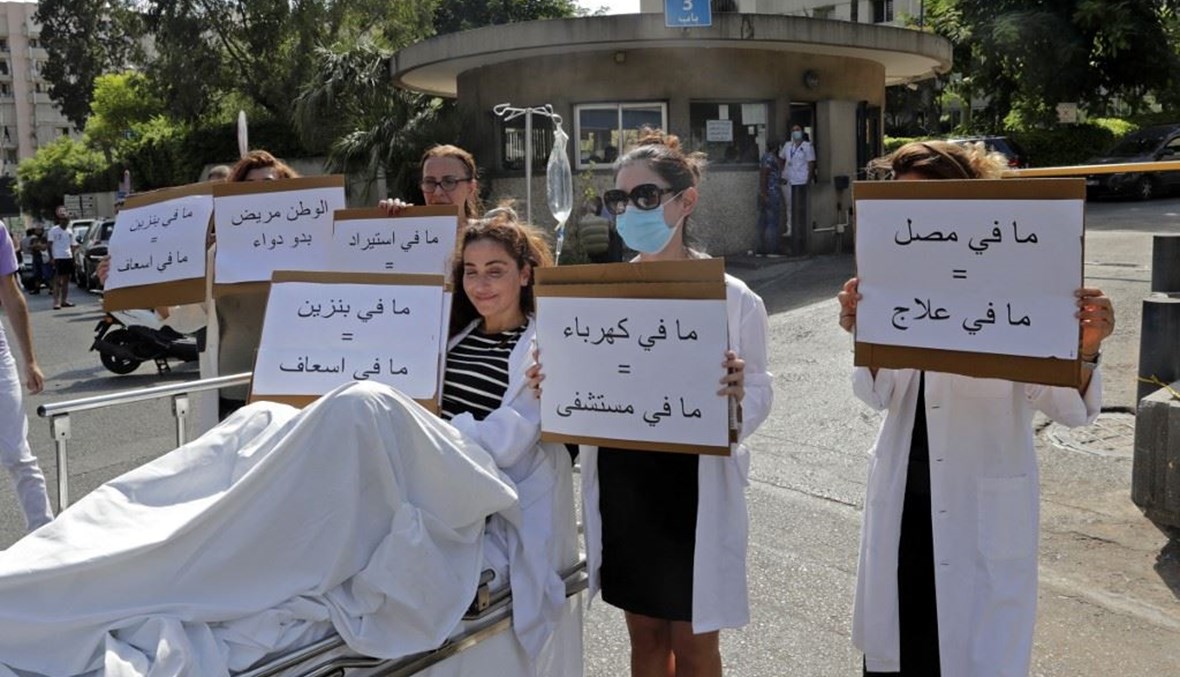 صيدلي يجلس على نقالة يحمل لافتة كتب عليها "لا بنزين = لا سيارة إسعاف" (أ ف ب). 