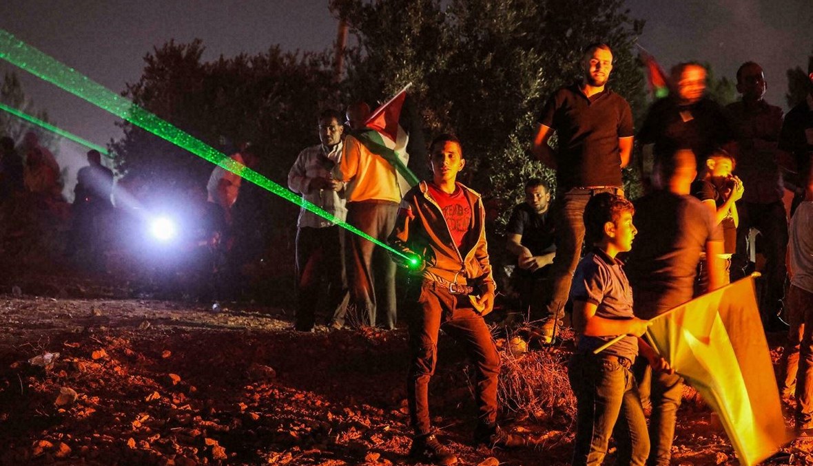 متظاهرون فلسطينيون في بيتا يوجهون أضواء ليزر خلال وقفة احتجاجية على بؤرة افيتار الاستيطانية الإسرائيلية في الضفة الغربية المحتلة (أ ف ب).