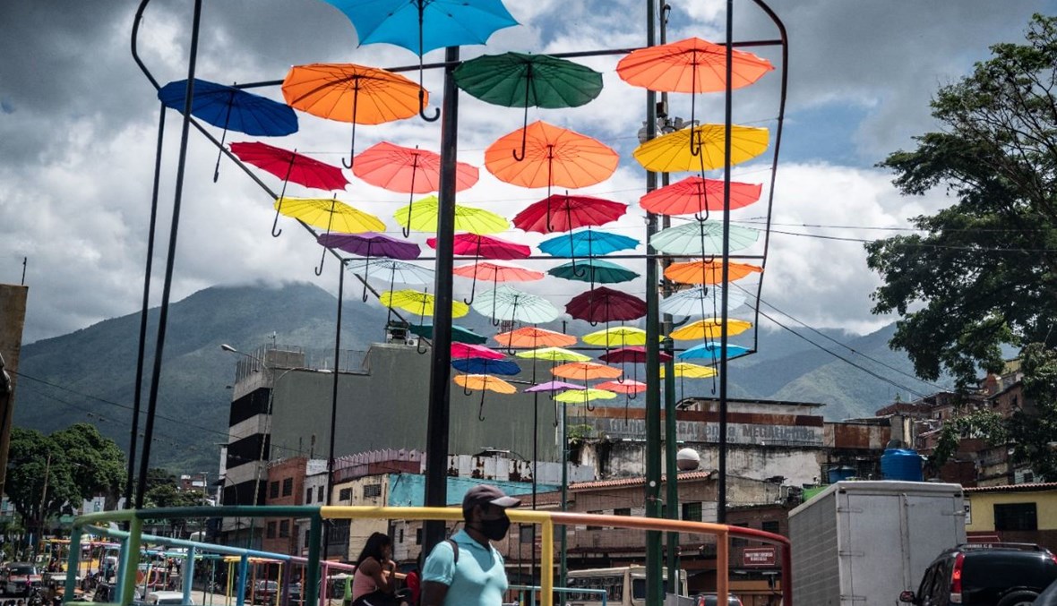 رجل يمر تحت مظلات ملونة خلال يوم غائم في كاراكاس (25 آب 2021، أ ف ب). 