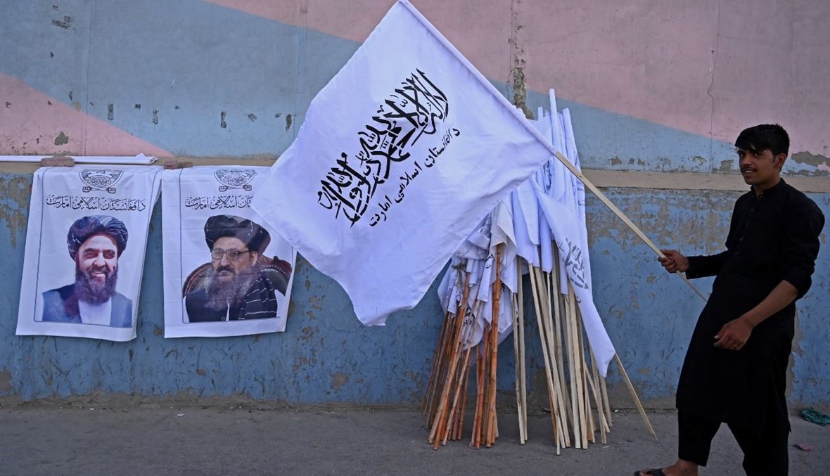 بائع يحمل علم طالبان بجوار ملصقات لقادة من الحركة بينما ينتظر بيعها في شارع في كابول (27 آب 2021، أ ف ب). 