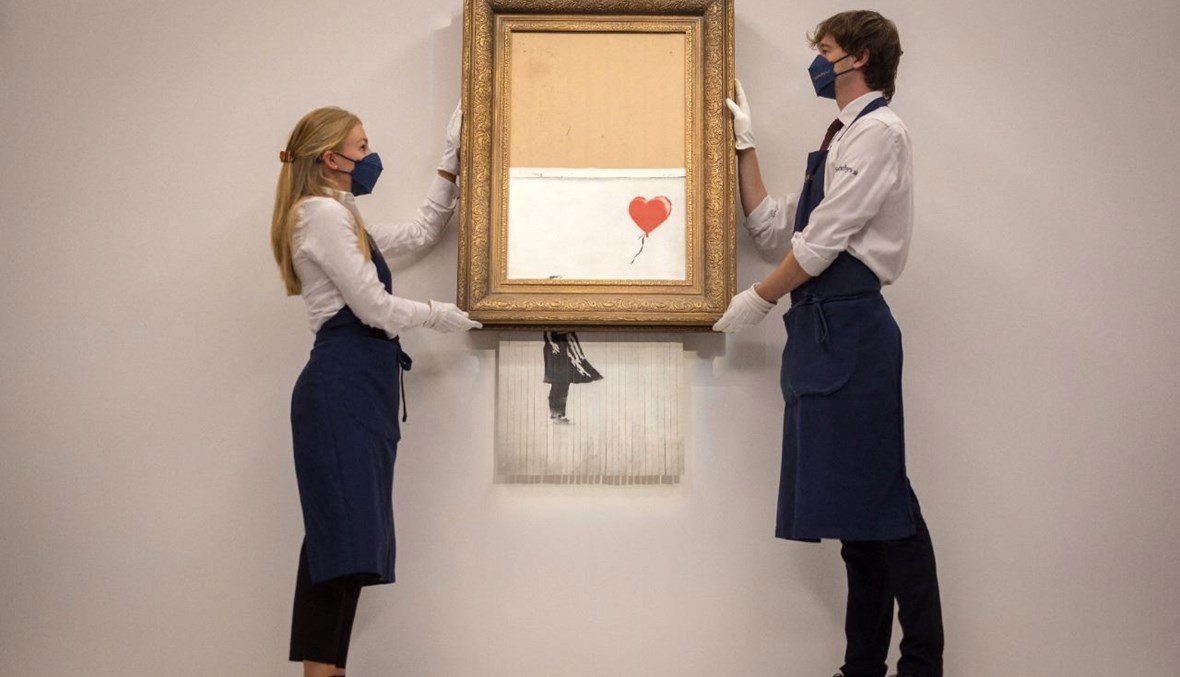 عاملان يحملان العمل الفني لبانكسي بعنوان Love is the Bin في دار مزادات سوثبي وسط لندن (3 أيلول 2021ـ أ ف ب). 