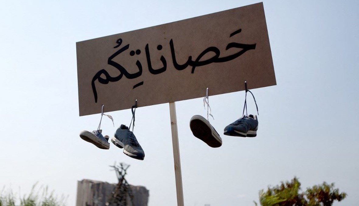  متظاهر يرفع لافتة وأحذية معلقة تحتها، خلال احتجاج في مرفأ بيروت (أ ف ب). 