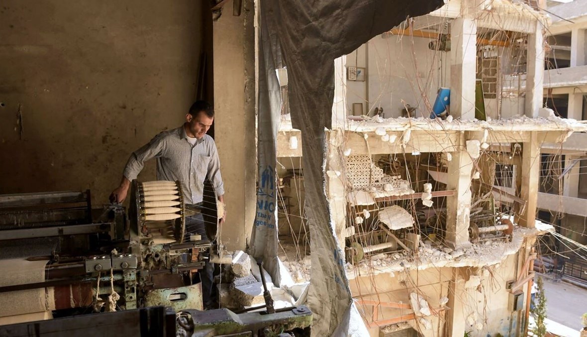 ورشة تعمل في مدينة حلب بينما لا يزال جزء منها مدمراً (أ ف ب).