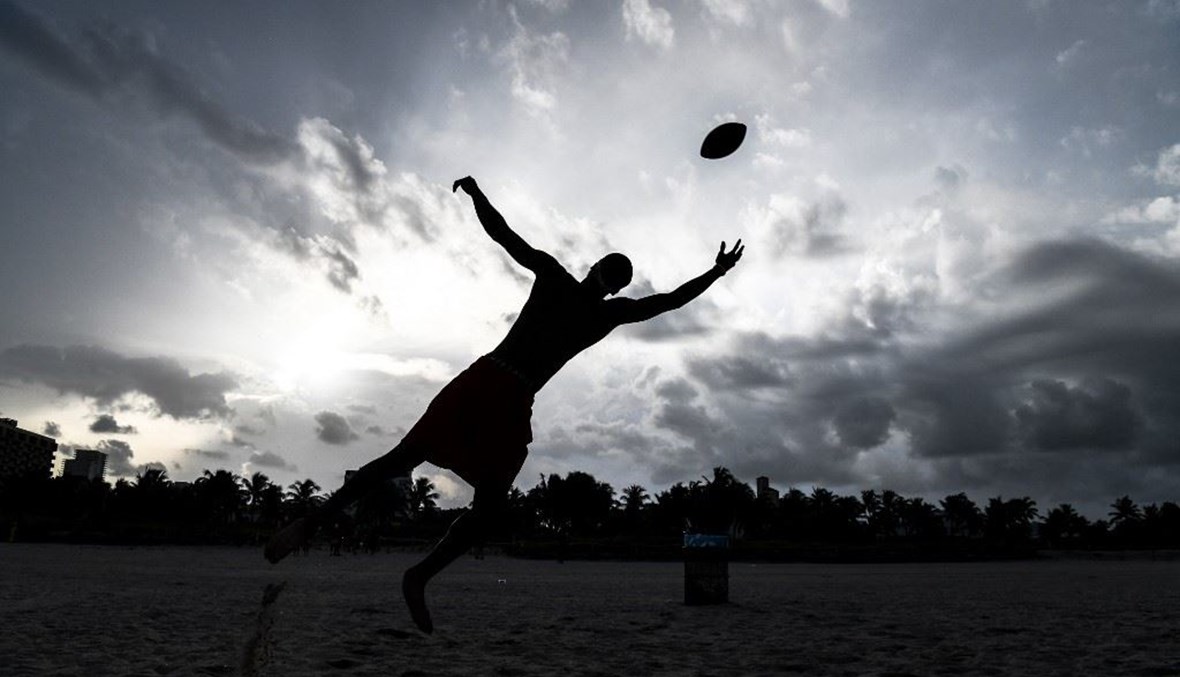 رجل يمسك كرة القدم على الشاطئ في ميامي (أ ف ب). 