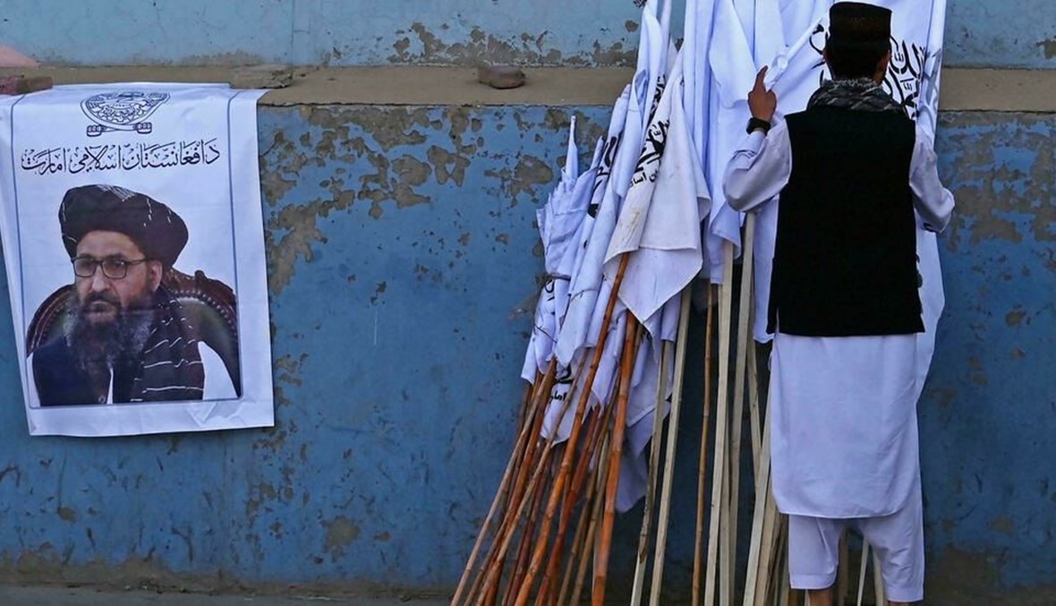 أفغاني يتفحصّ رايات لـ"طالبان" معروضة للبيع قرب صورة للقيادي عبد الغني برادر في أحد شوارع كابول (أ ف ب).