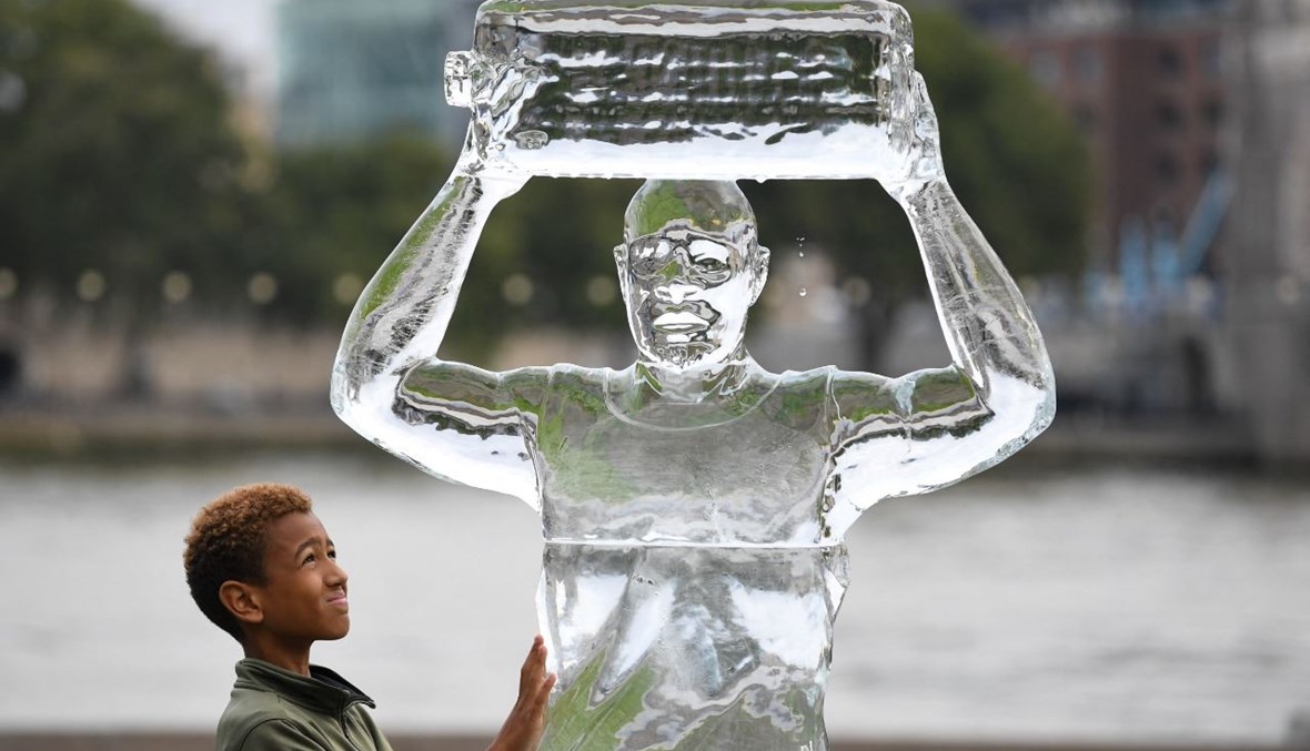 طفل وقف الى جانب منحوتة جليدية في لندن، تصور شخصا يجمع المياه لإظهار التهديد الذي يشكله تغير المناخ (15 ايلول 2021، ا ف ب).