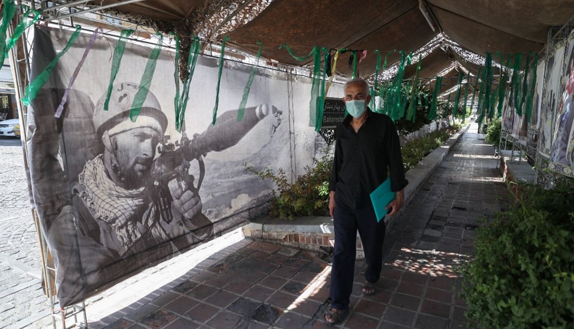 رجل يمر قرب رايات وضعت في اطار معرض شارع نظمه الجيش الإيراني وقوات الحرس الثوري في ساحة بهارستان في طهران، للاحتفال بـ"أسبوع الدفاع"  (25 ايلول 2021، أ ف ب).