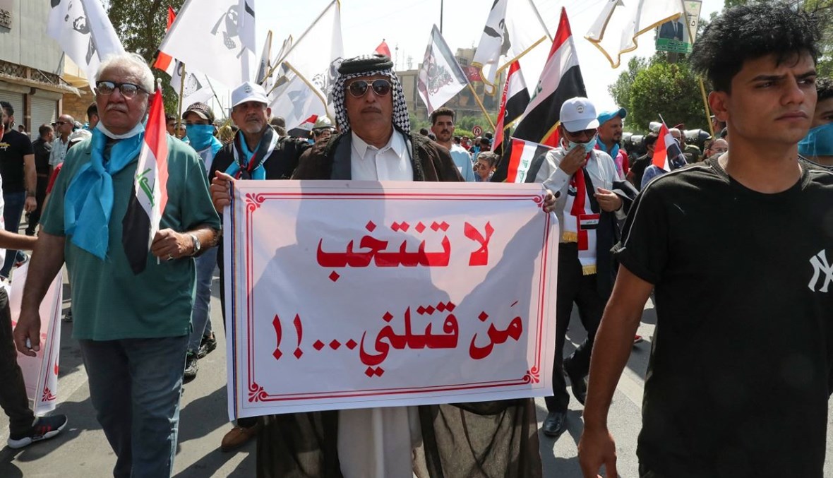 عراقيون يرفعون لافتات خلال تجمعهم في ساحة الفردوس وسط بغداد (1 ت1 2021، أ ف ب).