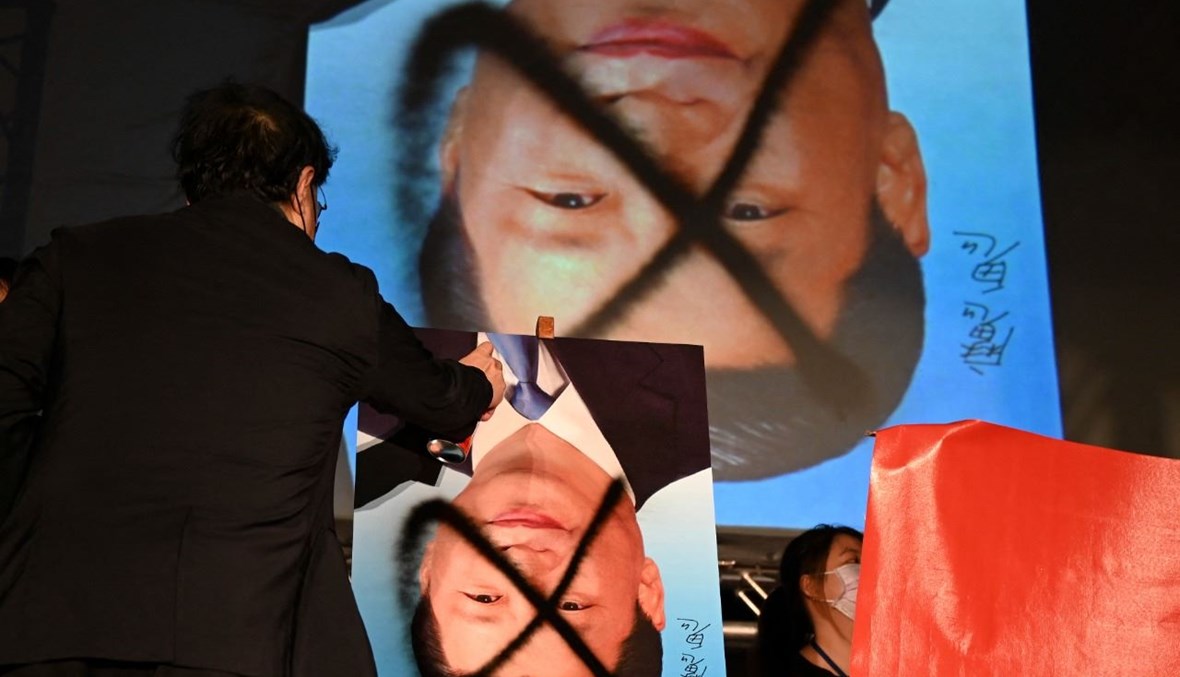 متظاهر يرش دهانا على صورة مقلوبة للرئيس شي أماما البرلمان في تايبيه، خلال مسيرة مناهضة للصين (1 ت1 2021، أ ف ب). 
