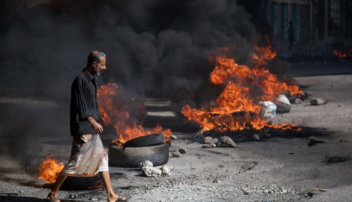 رجل يمني يمر بجوار الإطارات المحترقة خلال احتجاجات تطالب بإسقاط الحكومة (أ ف ب).