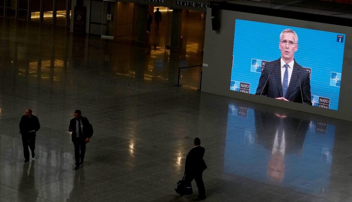 أشخاص يمرون قرب شاشة عملاقة يظهر عليها ستولتنبرغ متكلما خلال مؤتمر صحافي في مقر الناتو في بروكسيل (7 ت1 2021، أ ف ب). 