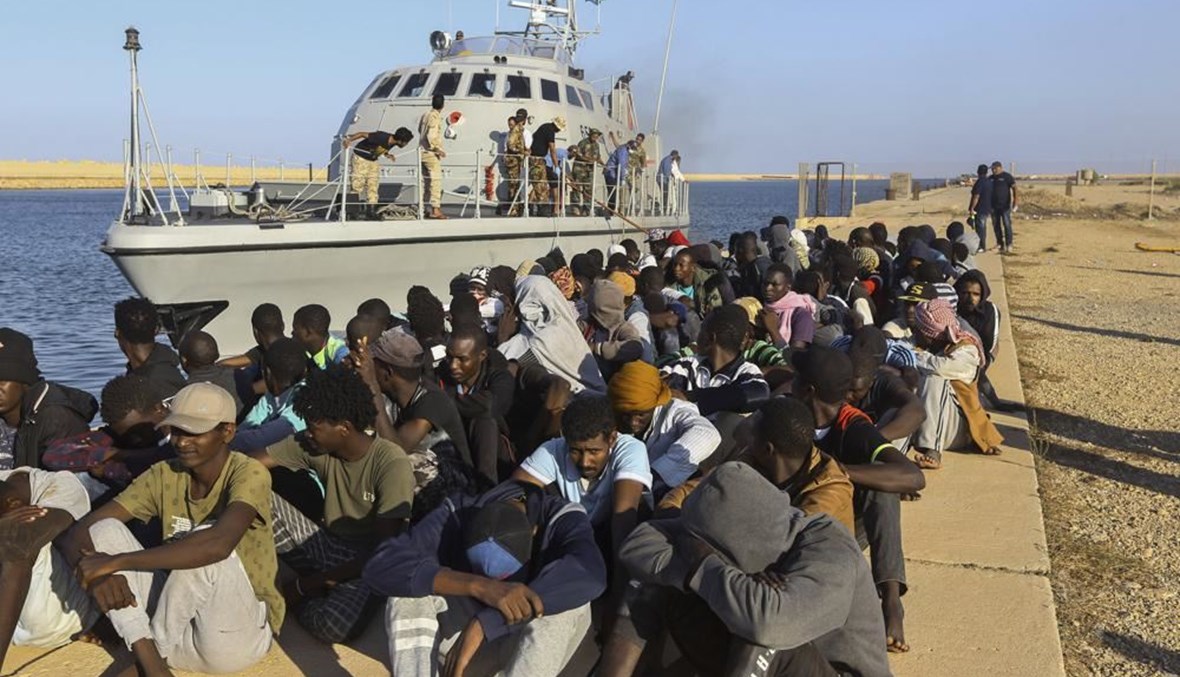 مهاجرون جلسوا بجوار قارب لخفر السواحل في مدينة الخمس بليبيا (1 ت1 2019، أ ب). 