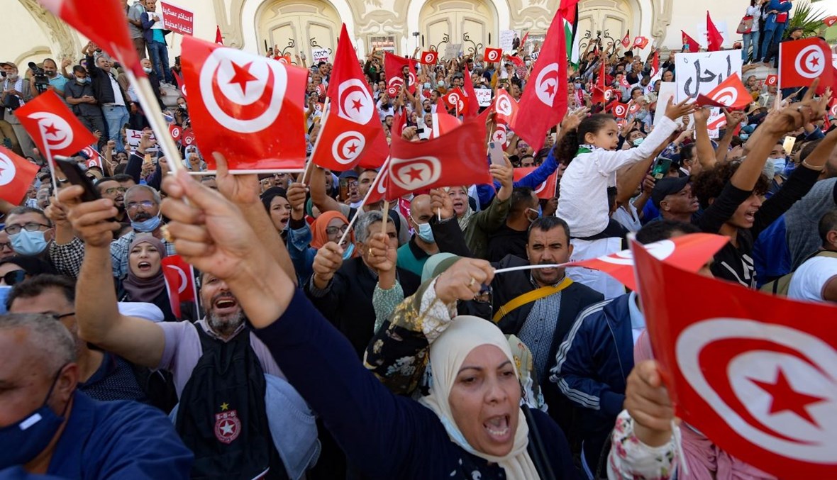 تونسيون يرفعون الأعلام الوطنية خلال مسيرة ضد سعيد في شارع الحبيب بورقيبة في العاصمة تونس (10 ت1 2021، أ ف ب). 