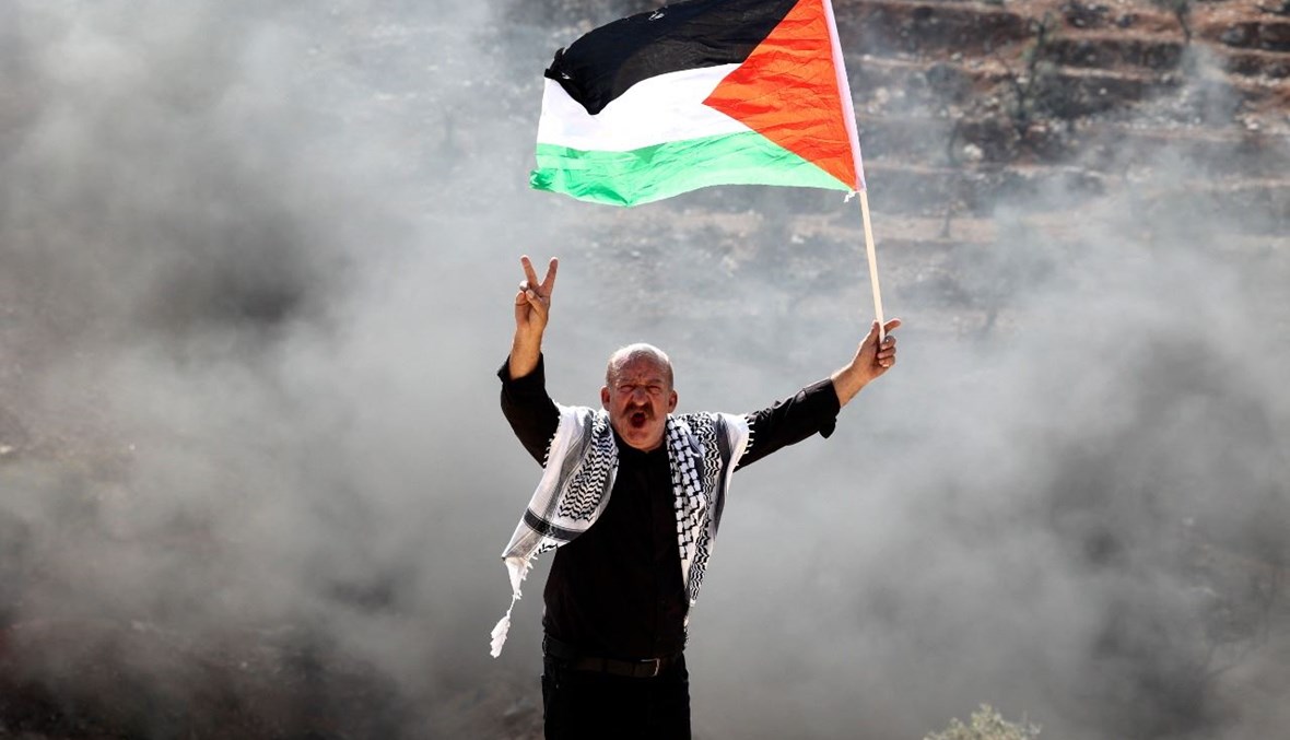 فلسطيني يرفع العلم الفلسطيني خلال تظاهرة ضد المستوطنات في قرية بيتا بالضفة الغربية المحتلة (15 ت1 2021، أ ف ب).