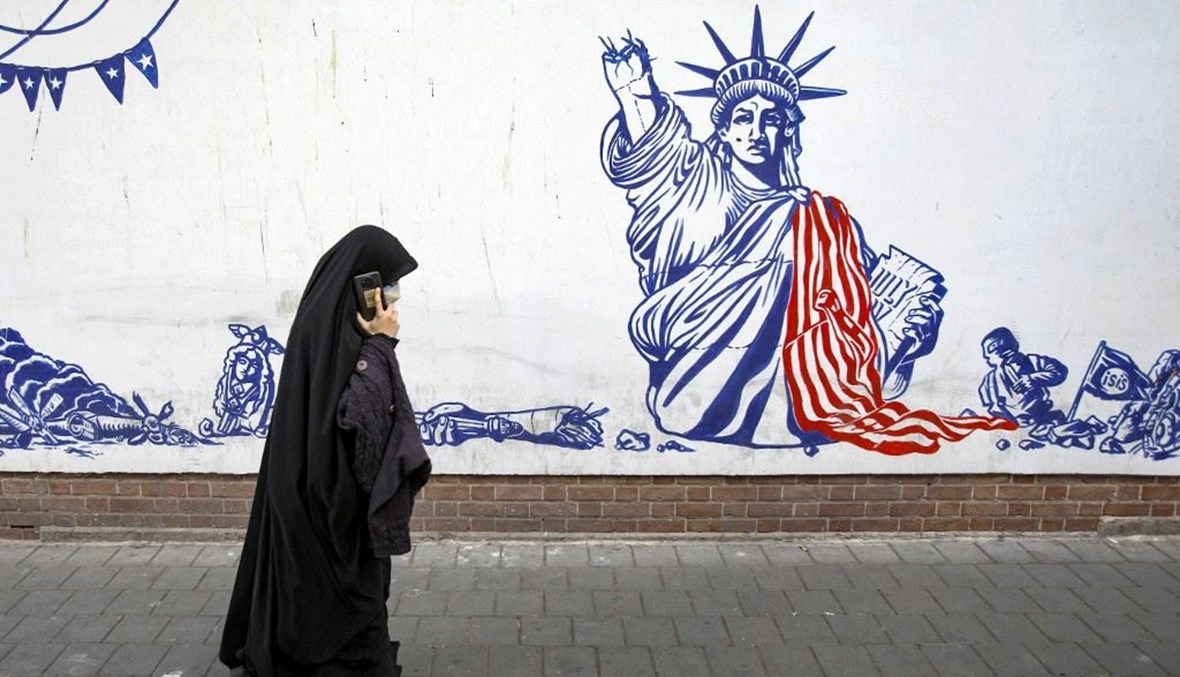  امرأة تستخدم هاتفها المحمول أثناء سيرها أمام السفارة الأميركية السابقة في العاصمة طهران (أ ف ب). 