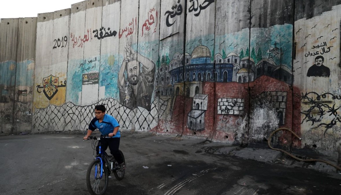طفل فلسطيني يركب دراجة قرب الجدار الإسرائيلي الفاصل في بلدة العيزرية بالضفة الغربية (8 ت2 2021، أ ف ب). 