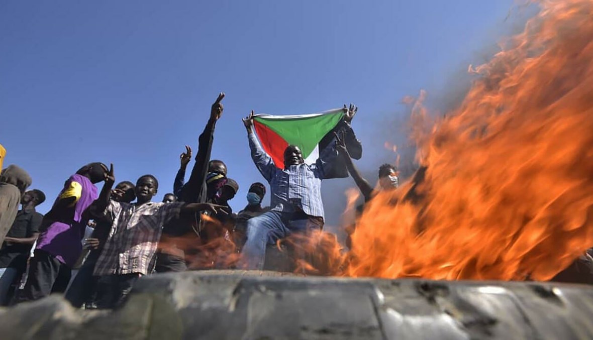 رجل يحمل علم السودان عند حاجز أضرمت فيه النار إلى شرق الخرطوم (أ ف ب).